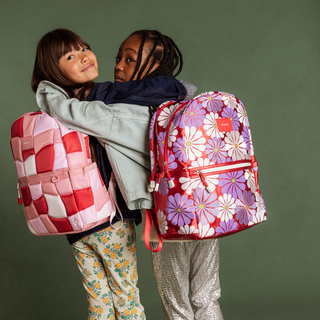 State Bags Kane Double Pocket Backpack - Ruby Floral Two children hugging with colorful backpacks against a green background