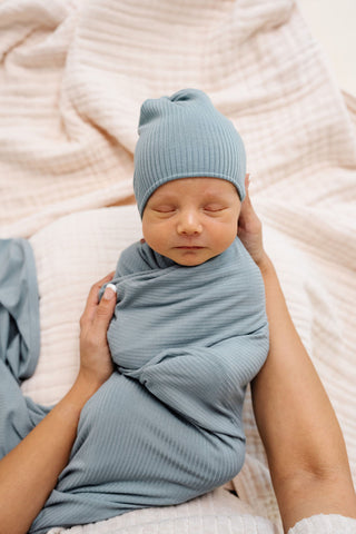 Lou Lou and Company Ribbed Swaddle Blanket - Ford
Newborn baby wrapped in a blue blanket and wearing a matching blue hat on a soft pink blanket.