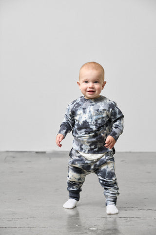 Little Bipsy Marble Pullover - Blue
Baby wearing a tie-dye outfit standing on a light wooden floor with a white wall background
