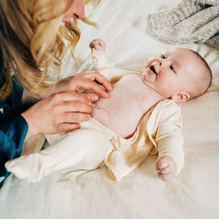 Bonsie Footie - Oat
Baby lying on a white blanket with a person adjusting the baby's diaper.