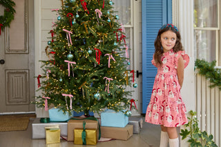 Pink Chicken Girls Jennifer Dress - Pink Candy Cane Santa
Young girl in a pink dress standing next to a decorated Christmas tree with presents underneath.