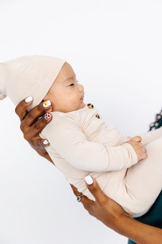 Lou Lou and Company Top Knot Hat - Winnie
Baby in a beige outfit being held by an adult against a white background