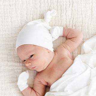 Lou Lou and Company Top Knot Hat - Finley
Newborn baby wearing a white hat and socks, lying on a soft surface.