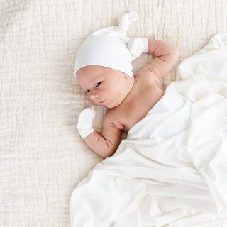Lou Lou and Company Swaddle Blanket - Finley
Newborn baby wrapped in white fabric with a matching hat and gloves on a textured white surface.