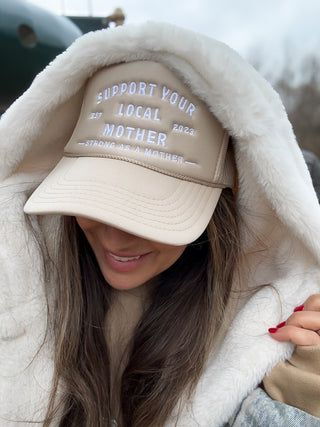 Support Your Local Mother® Trucker Hat - Tan
Person wearing a beige cap with text, wrapped in a white blanket.