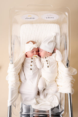 Lou Lou and Company Knotted Gown - Finley
Two babies in white outfits sitting in a high chair with a beige background