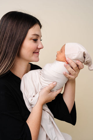 Lou Lou and Company Swaddle Blanket - Winnie
Woman holding a baby wrapped in a white blanket against a beige background