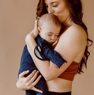 Bonsie Footie - Midnight Blue
Woman holding a baby wrapped in a blue wrap against a beige background