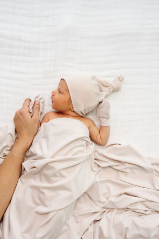 Lou Lou and Company Top Knot Hat - Winnie
Baby wrapped in a white blanket with a beige hat, lying on a white surface.