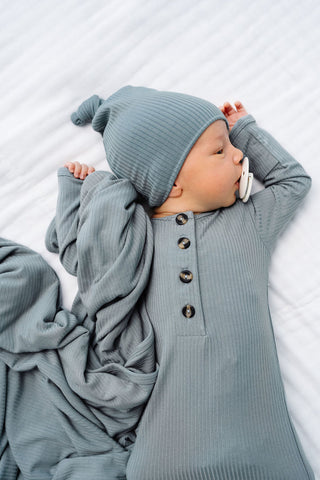 Lou Lou and Company Ribbed Knotted Gown - Ford
Baby in a gray outfit with buttons, lying on a white surface