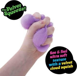 Schylling NeeDoh Wonder Waves Fuzz Ball Purple stress ball being squeezed by a hand with promotional text about its texture and brand.