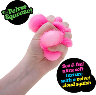 Schylling NeeDoh Flower Power Fuzz Ball Pink stress ball being held in a hand with 'The Velvet Squeeze' branding.