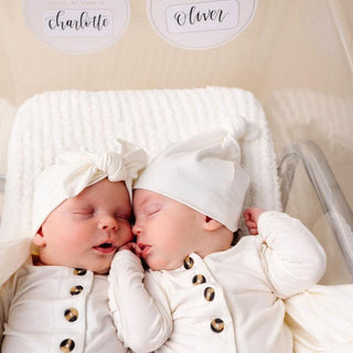 Lou Lou and Company Top Knot Hat - Finley
Two newborn babies in white outfits with hats, lying next to each other on a blanket.