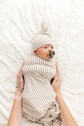 Lou Lou and Company Ribbed Swaddle Blanket - Indy
Newborn baby wrapped in a striped swaddle with a pacifier, wearing a matching hat, held by a person on a soft white background.