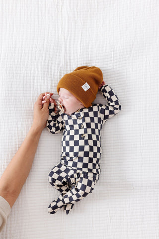 Lou Lou and Company Top and Bottoms - Gibson
Baby wearing a checkered outfit and orange hat lying on a white textured surface