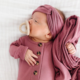 Lou Lou and Company Top and Bottoms - Marjorie
Newborn baby in a pink outfit with a matching turban and blanket, holding a teething ring.