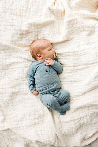 Lou Lou and Company Ribbed Top and Bottoms - Ford
Newborn baby in a blue outfit lying on a textured white blanket