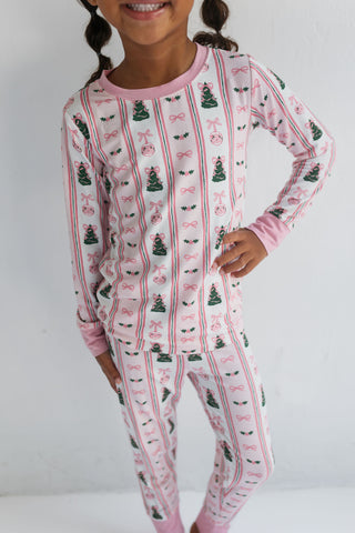 In My Jammers Pinkmas Two Piece Set 
Child wearing a festive pajama set with Christmas tree and bow pattern on a plain background