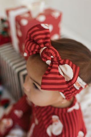 Baby wearing a red and white striped headband with a blurred background of wrapped gifts.