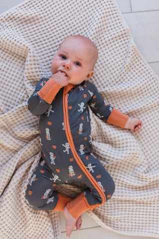 In My Jammers Mummy Zipper Romper Baby in a dark gray onesie with orange accents lying on a textured beige blanket.