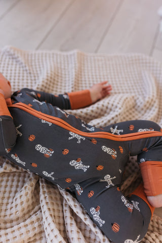 In My Jammers Mummy Zipper Romper Baby in a dark outfit with orange accents lying on a textured blanket
