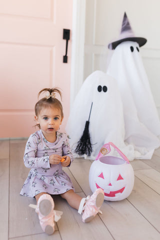 In My Jammers Ballerina Ghost Twirl Bodysuit Child in a floral dress sitting next to a large inflatable ghost and a pumpkin lantern indoors.