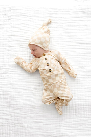 Lou Lou and Company Top and Bottoms - Austin
Baby in a checkered outfit and hat lying on a white textured surface