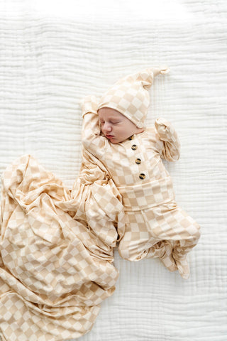 Lou Lou and Company Top and Bottoms - Austin
Newborn baby wrapped in a beige swaddle with a matching hat on a white textured surface