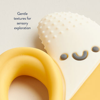 Itzy Ritzy Chew Crew® - Banana Silicone teether with textured surface and smiling face design on a light background.