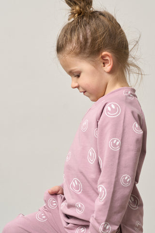 Little Bipsy Smiley Pullover - Dusty Purple
Child wearing a pink outfit with smiley face patterns on a plain background