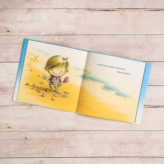 I Wish You More Hardcover Book
Open book with an illustration of a child on a beach, on a wooden surface.