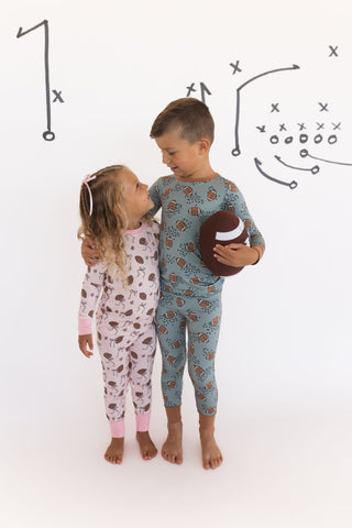 In My Jammers Blush Football Two Piece Set
Two children in pajamas standing next to each other with a football, against a white background with sports graphics.