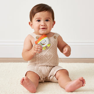 Itzy Ritzy Sweetie Shake Plus Teething + Rattle Toy - Sushi Baby sitting on a white surface holding a colorful toy