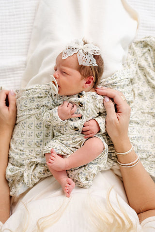 Lou Lou and Company Knotted Gown - Etta
Newborn baby wrapped in a patterned blanket with a lace headband, held by a person.