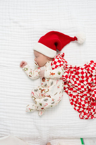 Lou Lou and Company Santa Beanie
Newborn baby wearing a Santa hat and Christmas-themed outfit on a white striped background