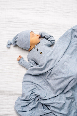 Lou Lou and Company Knotted Gown - Crew
Newborn baby in a blue outfit and hat lying on a white textured surface