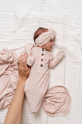 Lou Lou and Company Knotted Gown - Flora
Baby in a pink floral outfit and headband lying on a textured white surface.