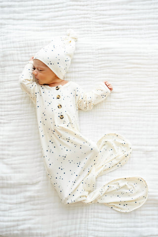 Lou Lou and Company Knotted Gown - George
Newborn baby in a white outfit with black polka dots and matching hat, lying on a white textured surface.