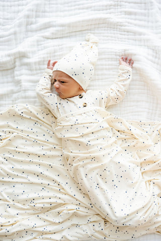Lou Lou and Company Swaddle Blanket - George
Newborn baby swaddled in a white blanket with black dots on a textured white background