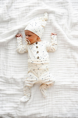 Lou Lou and Company Top and Bottoms - George
Baby lying on a white textured blanket wearing a white outfit with buttons and a matching hat.