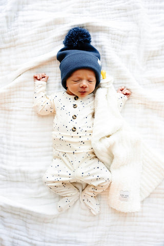 Lou Lou and Company Top and Bottoms - George
Newborn baby wrapped in a blanket with a blue hat on a white textured surface