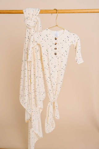 Lou Lou and Company Knotted Gown - George
White baby outfit with buttons and a matching wrap on a beige background