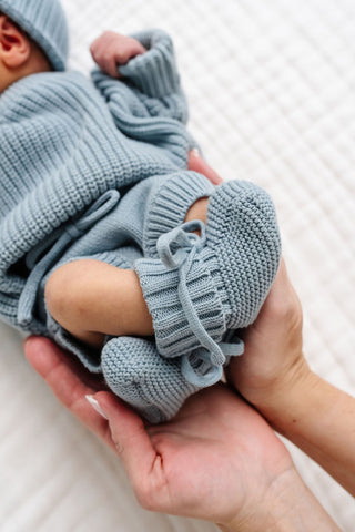 Lou Lou and Company Knit Booties - Steele
Newborn baby in a blue knitted outfit being held on a white background
