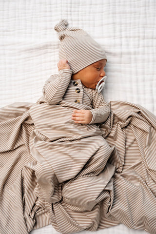 Lou Lou and Company Knotted Gown - Banks
Newborn baby wrapped in a striped swaddle and wearing a matching hat on a white blanket.