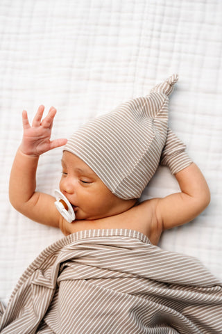 Lou Lou and Company Top Knot Hat - Banks
Newborn baby wearing a striped hat and swaddle on a white blanket