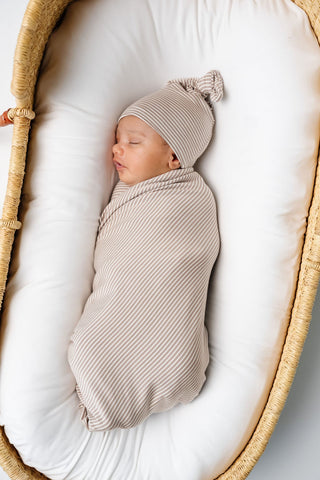 Lou Lou and Company Swaddle Blanket - Banks
Newborn baby swaddled in a beige blanket and wearing a matching hat, sleeping in a wicker basket.
