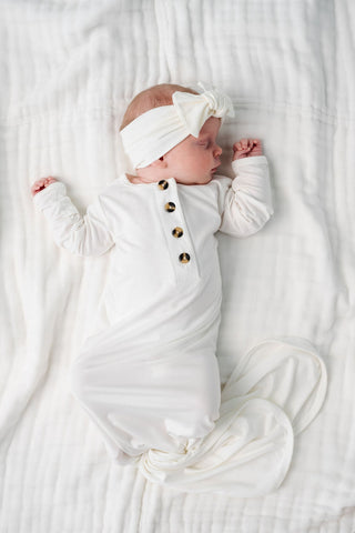 Lou Lou and Company Knotted Gown - Finley
Newborn baby wrapped in a white swaddle with a headband on a white blanket