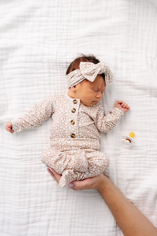 Lou Lou and Company Top and Bottoms - Laynie
Newborn baby in a floral outfit lying on a white textured blanket with a hand holding the baby's foot.