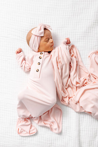 Lou Lou and Company Knotted Gown - Sophie
Newborn baby in pink outfit and headband lying on a white textured surface