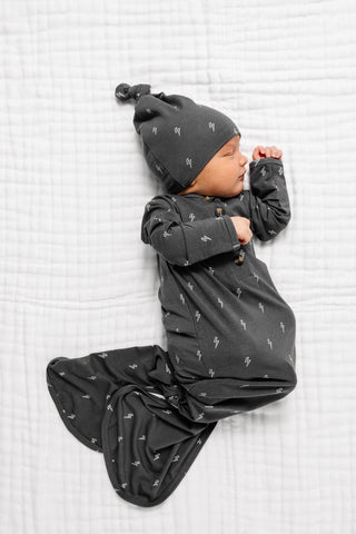 Lou Lou and Company Top Knot Hat - Everett
Baby in dark gray outfit with lightning bolt pattern lying on a white textured surface